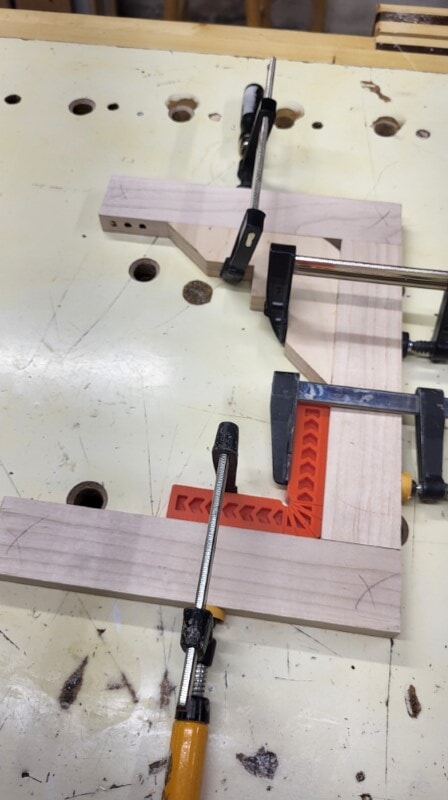 Woodworker clamping a board square using a shop-made corner jig and commercial clamp