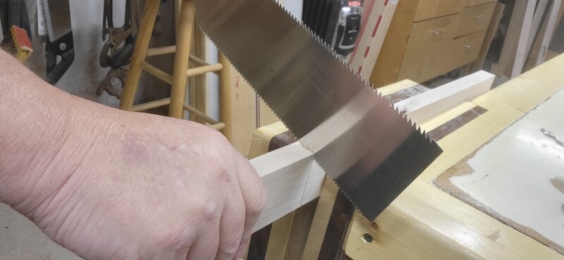 Close-up of a Japanese hand saw cutting along a marked line on a clamped board