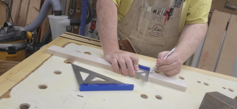 Marking a square layout line across a board Woodworker using a small speed square and mechanical pencil to draw a layout line across a narrow board