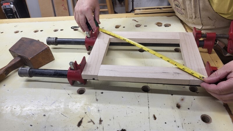 Tape measure stretched diagonally from corner to corner to check square on a wood panel