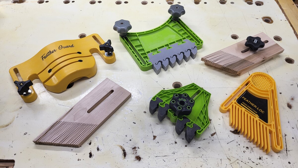 Collection of purchased and homemade featherboards on a workbench, showing different designs used to keep boards tight against the fence for safer, accurate cuts