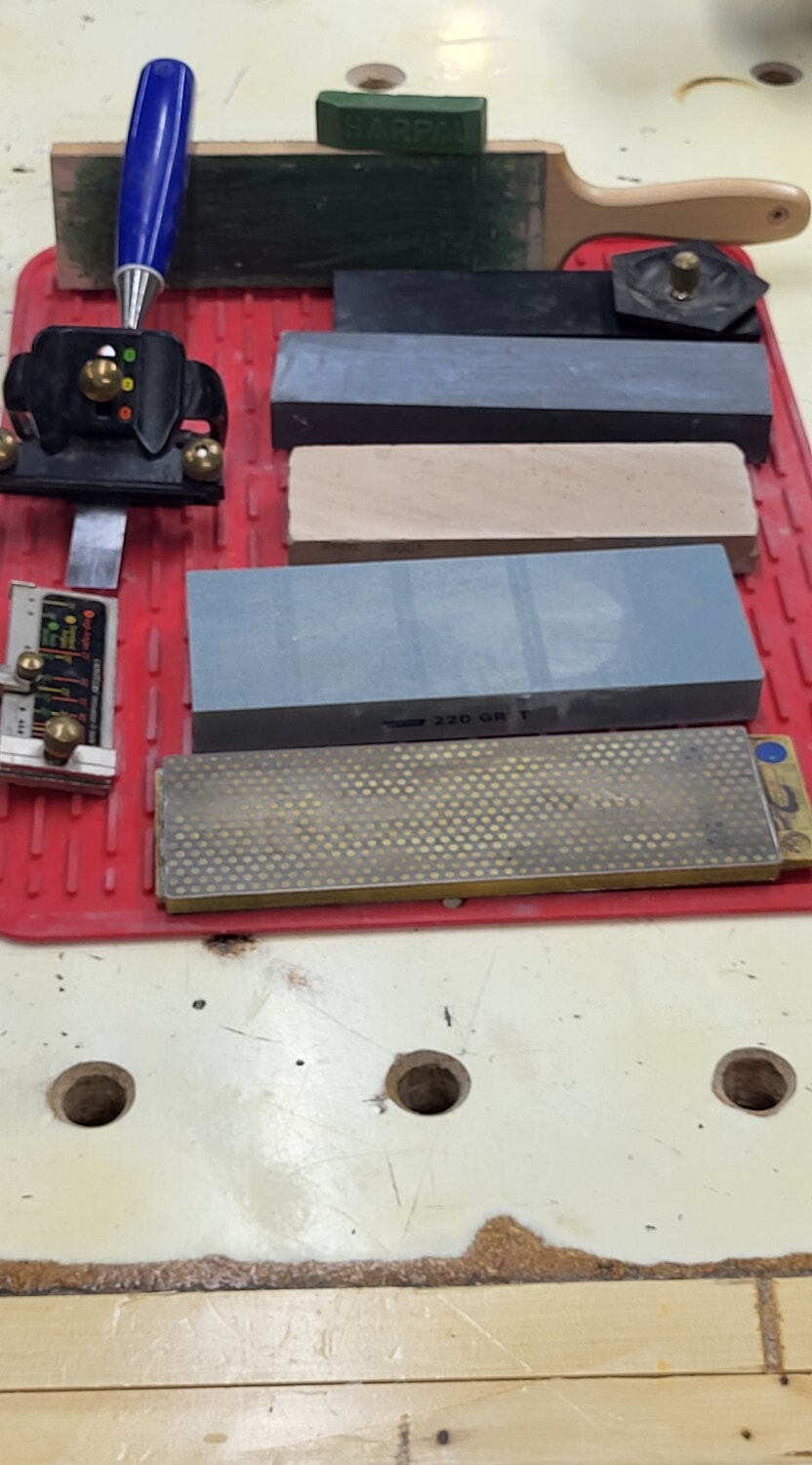 Collection of sharpening equipment including honing guides, water stones, diamond plate, and strop, showing how simple sharpening setups keep woodworking tools sharp and safe