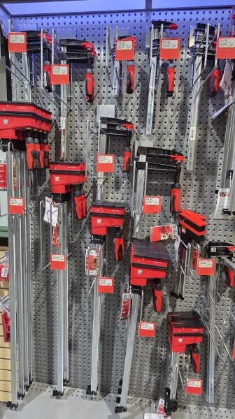 Wall of Bessey parallel clamps and bar clamps displayed on a pegboard at Woodcraft.