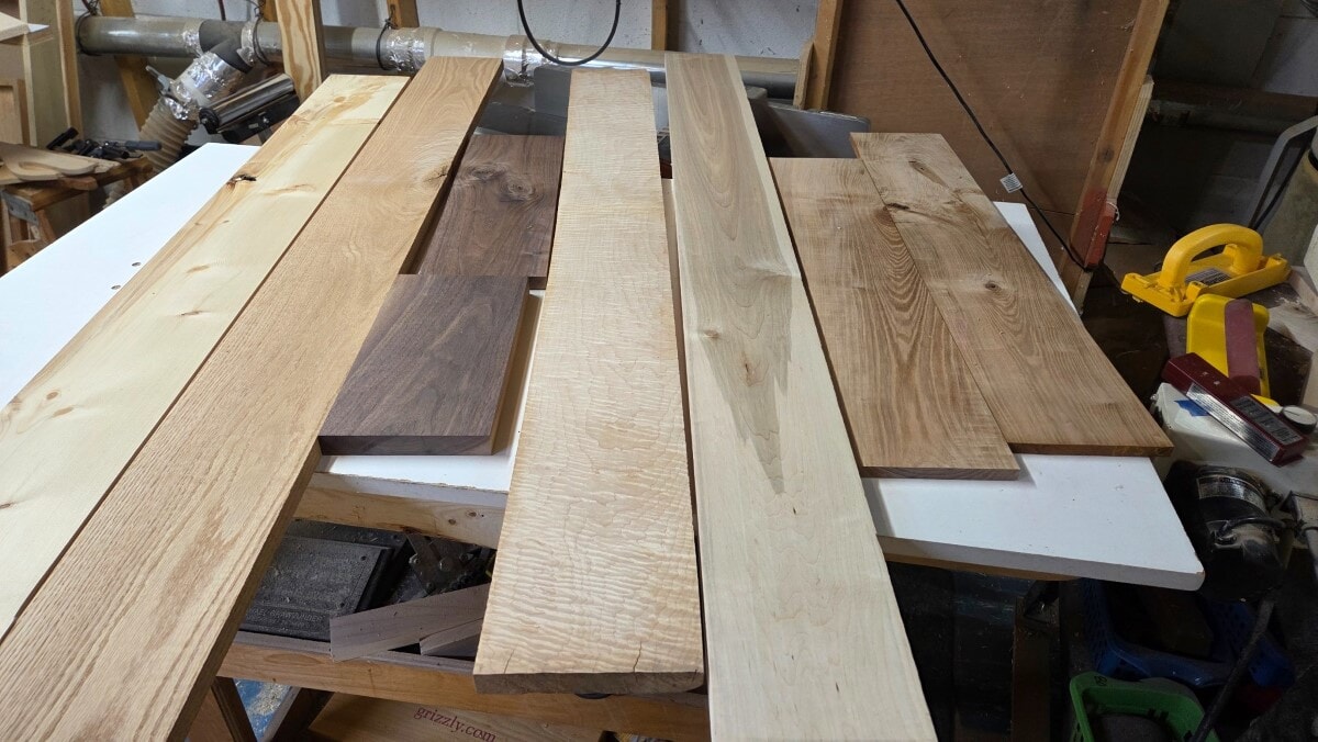 Domestic hardwood and softwood boards including Pine, Oak, Walnut, Curly Maple, Soft Maple, and Ash arranged on a workbench in The Master’s Workshop of WI.