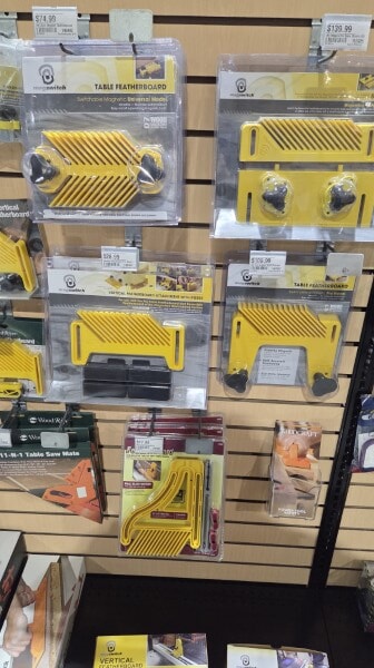 Yellow featherboards and hold-downs displayed in retail packaging on a Woodcraft wall rack.