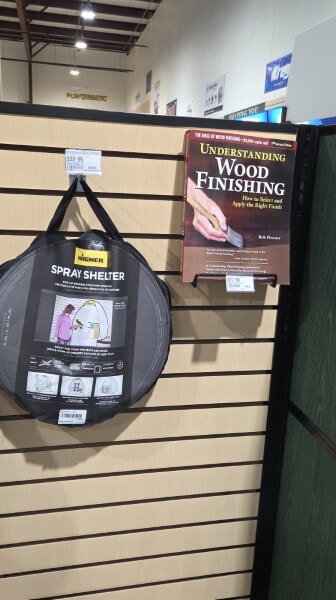 Display of a wood finishing book and a HomeRight Small Spray Shelter hanging on a Woodcraft wall.