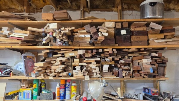 Shelf of assorted small wood pieces in a workshop, organized and labeled by species and size.