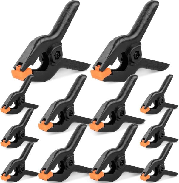 Assorted set of black spring clamps with orange pivoting pads arranged in multiple sizes.